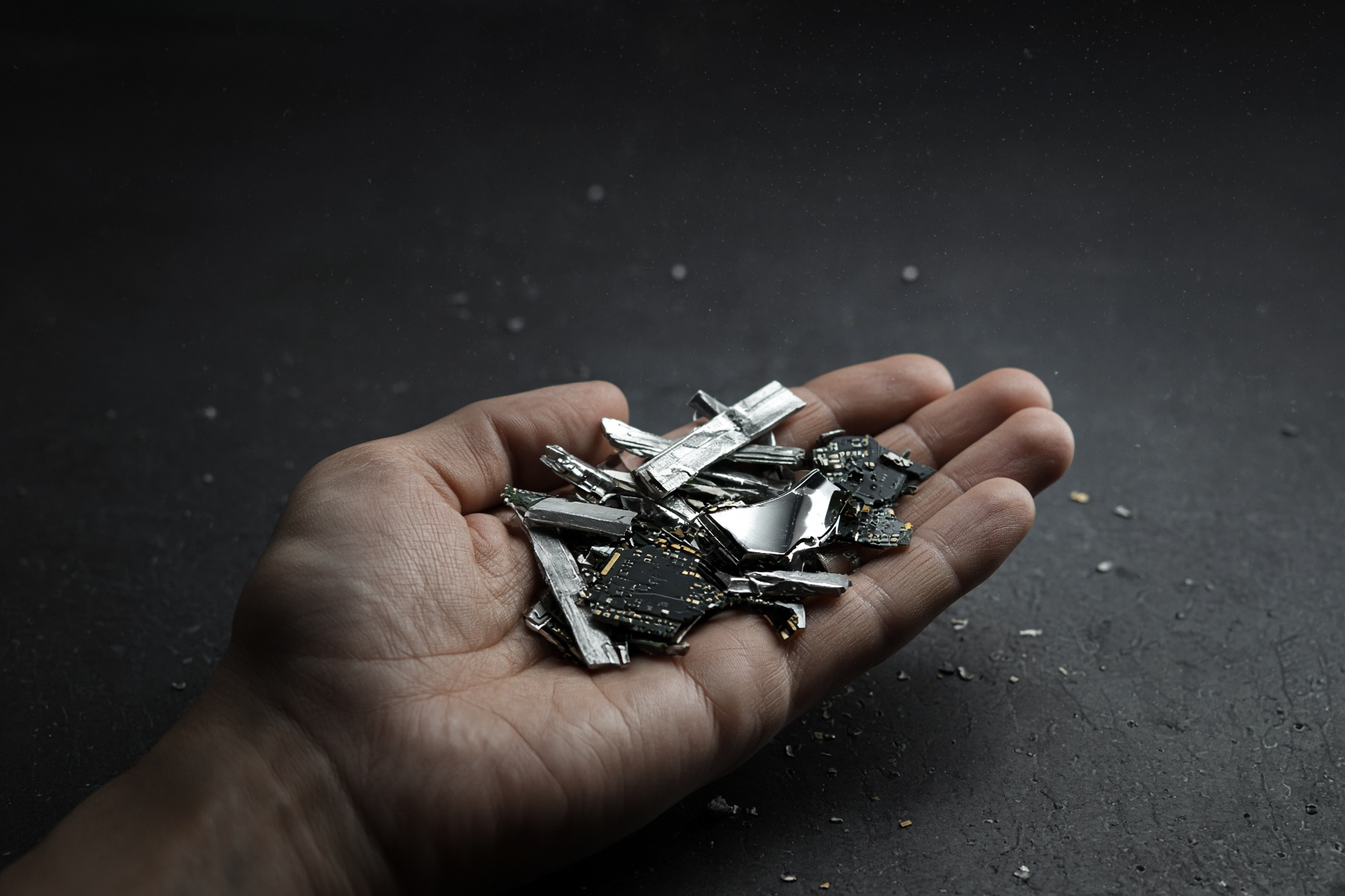 An open palm holding a pile of shredded drive fragments about 12 mm across: torn aluminium, circuit board pieces and a shard of platter.